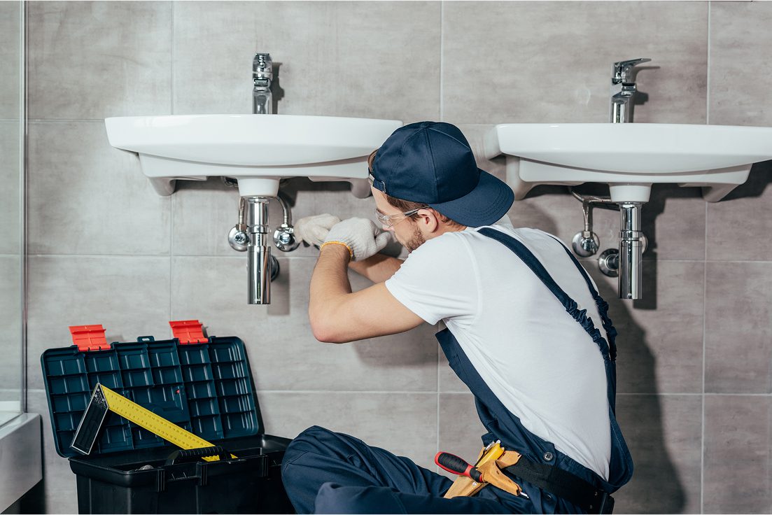 Plumber repairing sink with toolbox nearby.