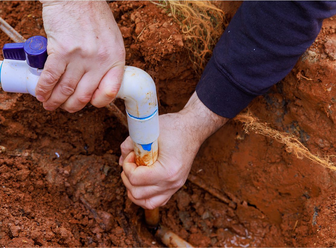 Hands repairing underground water pipe leak.
