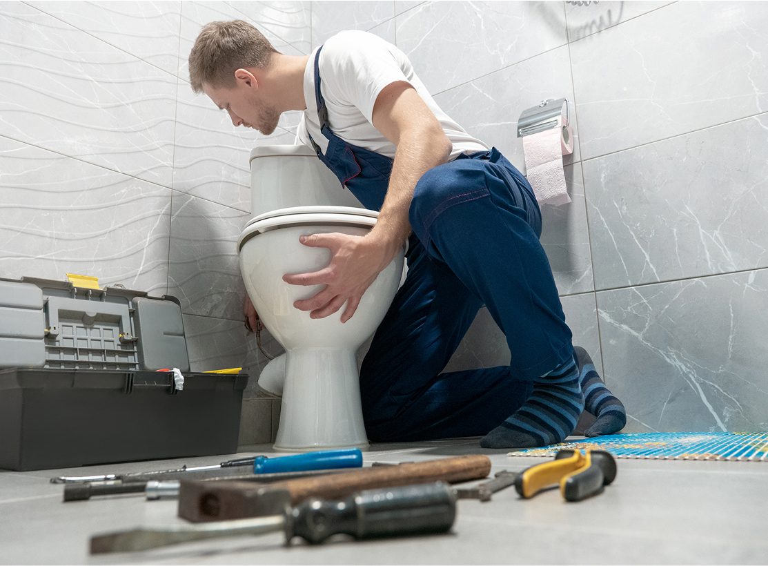 Plumber fixing toilet in bathroom.