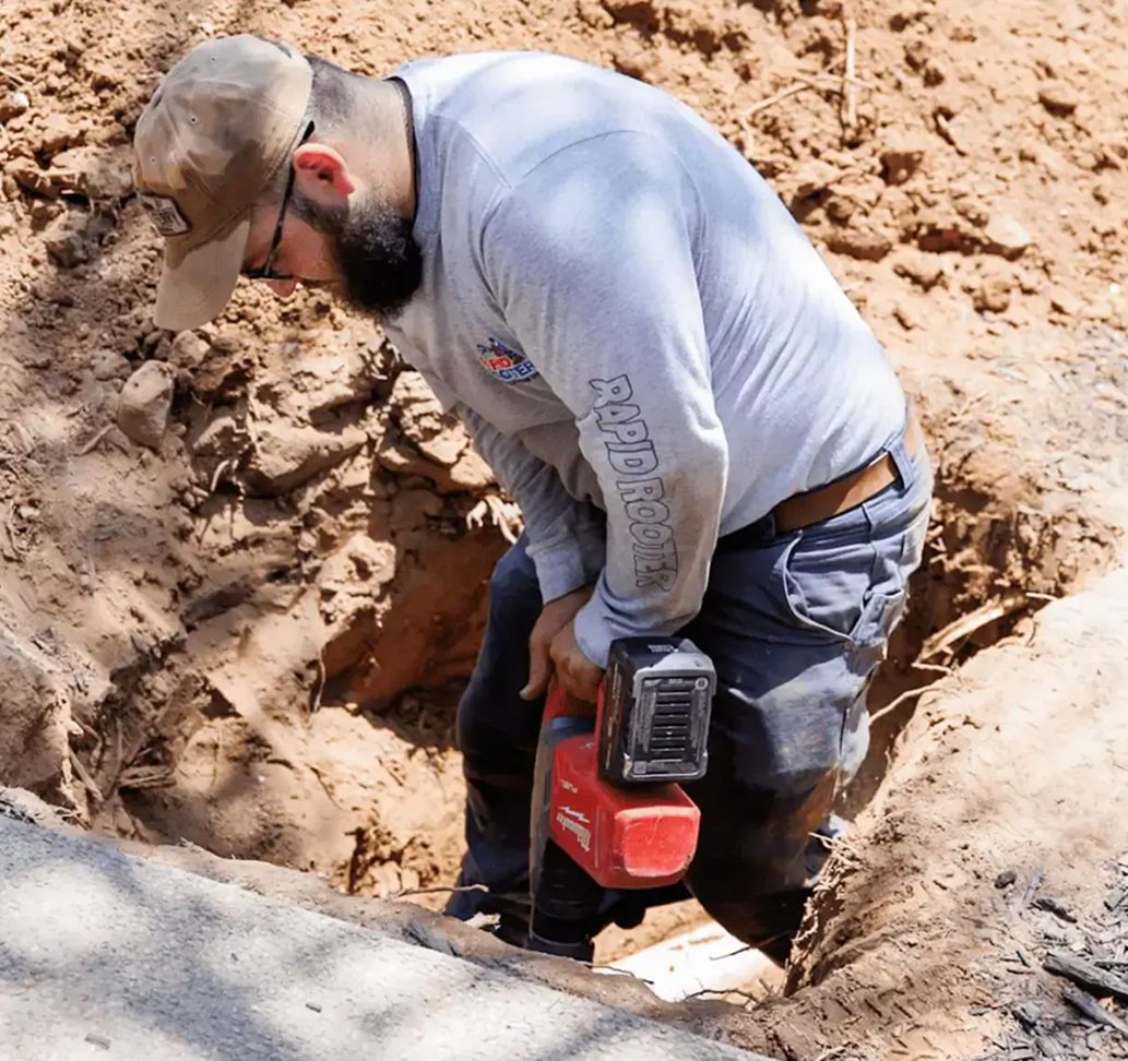 Worker operating a power tool in trench.