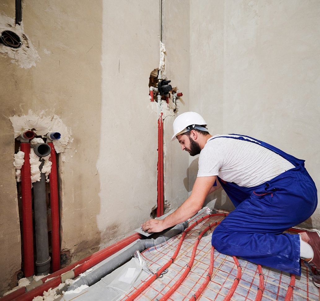 Worker installing floor heating system pipes.