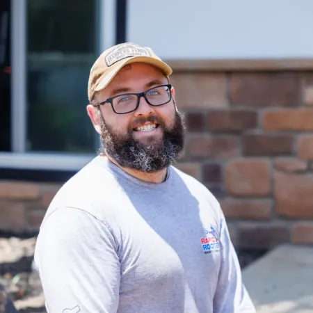 Smiling man with beard wearing glasses outdoors.