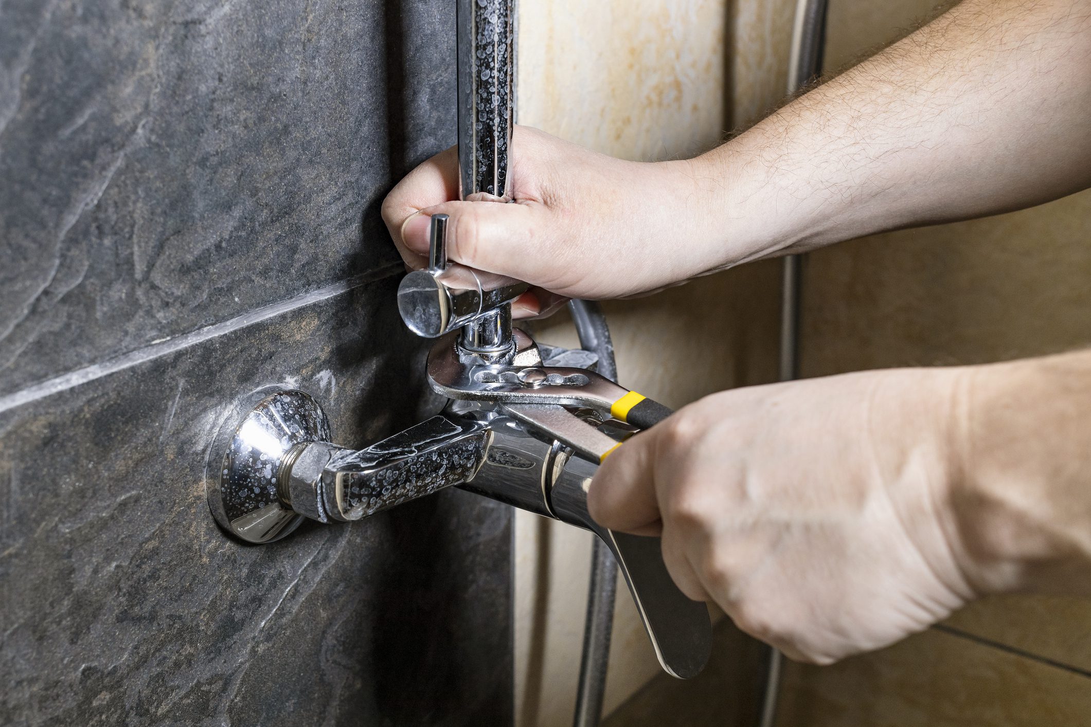 plumber fixes old shower faucet on tiled wall at home