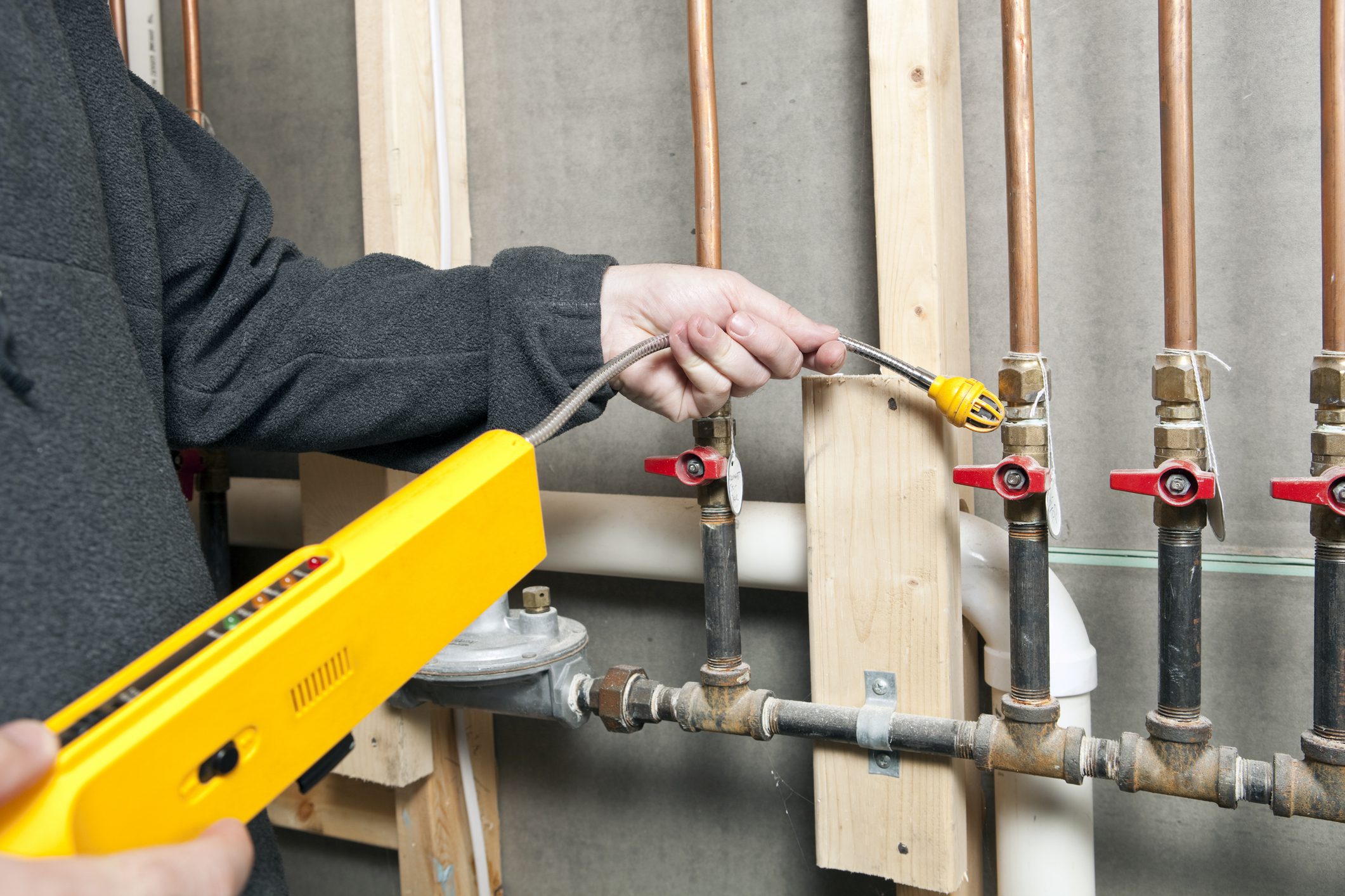 A worker is using a leak detector near a set of house gas lines at a renovation site. Very small gas leaks are often found at pipe joints in older construction.